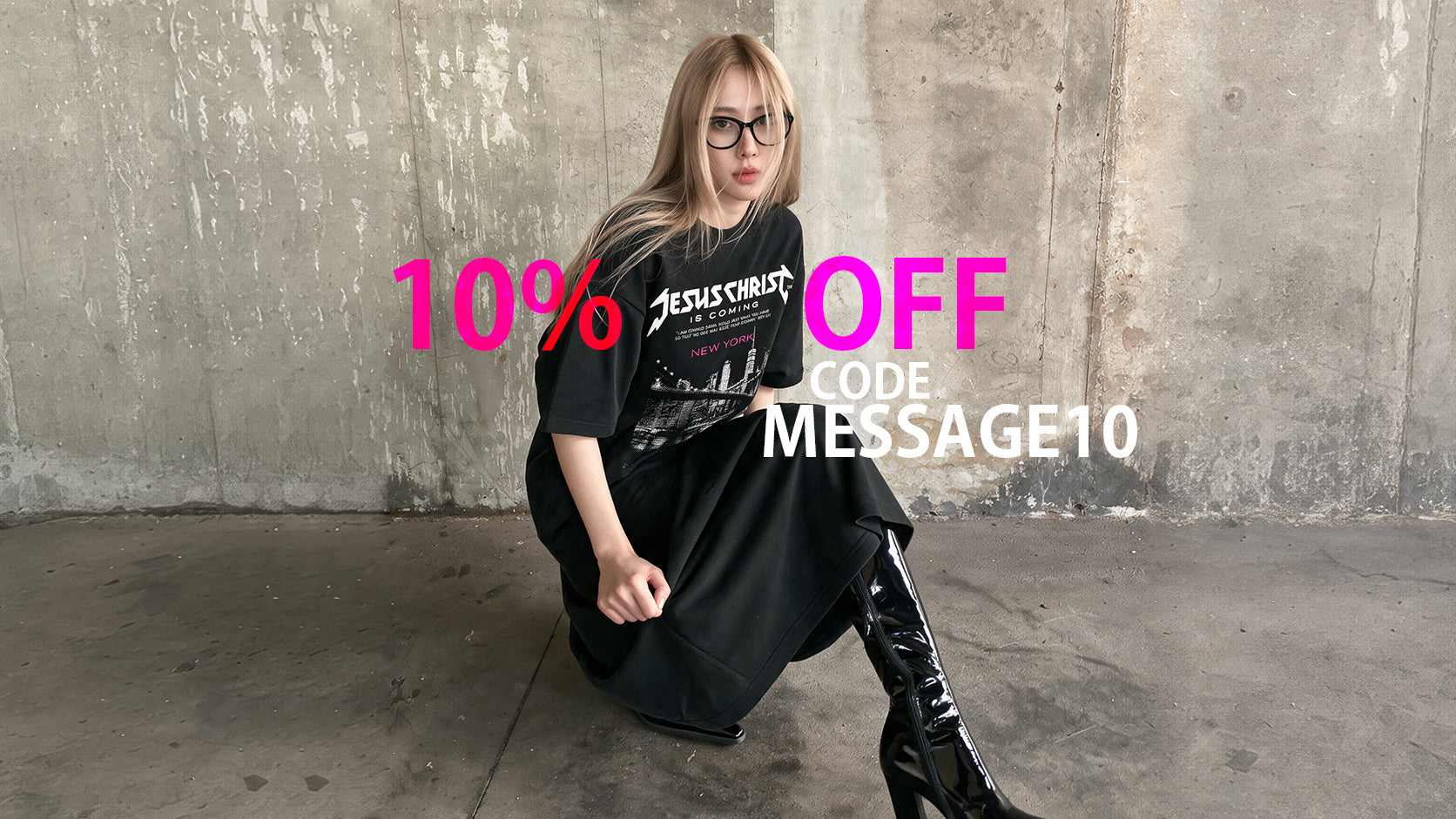 A woman wearing a premium christian black graphic t-shirt and black leather boots poses against a concrete wall, with a sale overlay reading '10% OFF CODE MESSAGE10'.